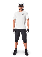 Mountain biker uomo con pantaloncini Alpinestars A-Aria neri, maglia tecnica bianca, casco bianco e protezioni per le ginocchia nere, equipaggiamento professionale da ciclismo fuoristrada in vista frontale a figura intera