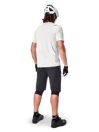 Mountain biker visto da dietro con pantaloncini Alpinestars A-Aria in nero, maglia tecnica bianca a maniche corte, casco bianco, guanti neri e scarpe da mountain bike nere, abbigliamento da ciclismo per trail riding