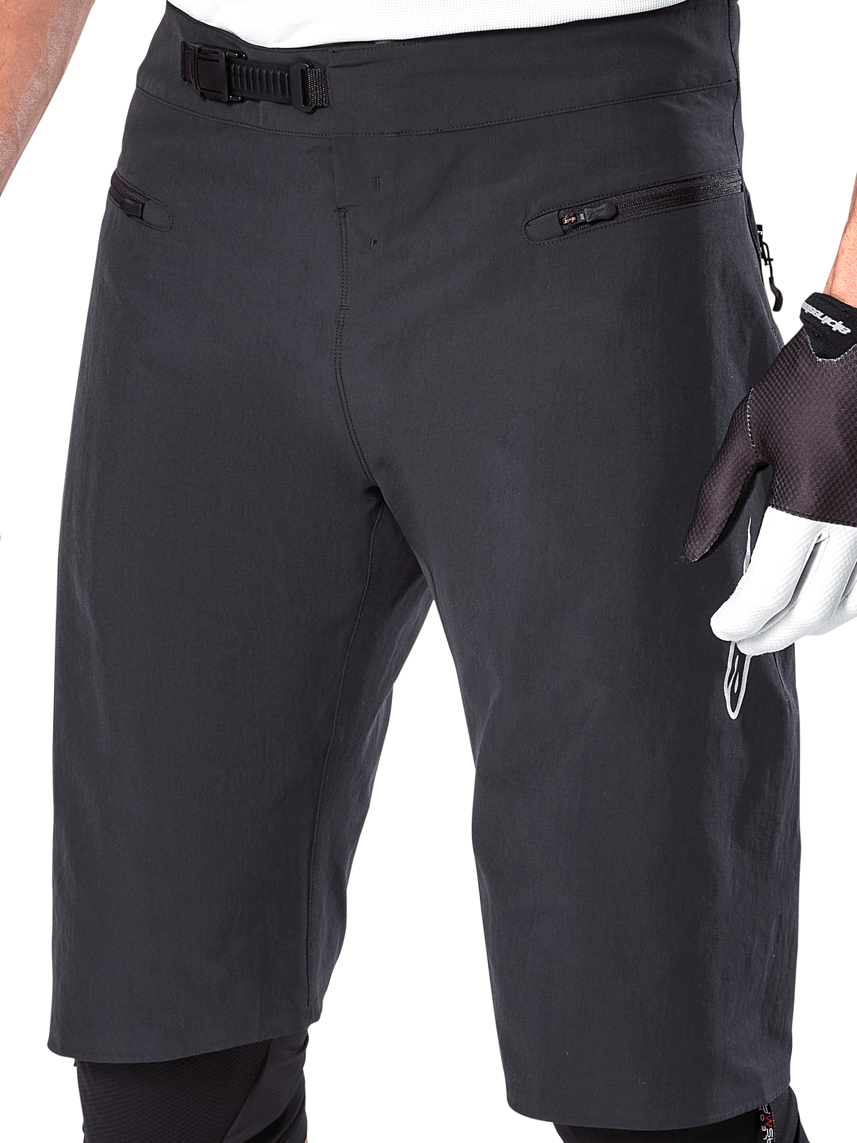 Alpinestars A-Aria Shorts, pantaloncini da mountain bike, nero, vista ravvicinata della vita anteriore e delle cosce che mostra il sistema di chiusura a cricchetto e le tasche con zip, indossati con guanti da ciclismo bianchi e neri, abbigliamento tecnico da trail