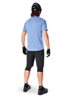Alpinestars A-Dura Elite Shorts, pantaloncini da mountain bike, nero, vista posteriore su modello, indossati con maglia azzurra a maniche corte e attrezzatura protettiva nera, design tecnico con tasche con zip e dettagli riflettenti per il ciclismo fuoristrada