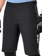 Pantaloncini Alpinestars A-Dura Elite, pantaloncini MTB neri, vista ravvicinata con chiusura frontale a scatto e tasca laterale con zip, indossati da un ciclista con guanti neri e ginocchiere, abbigliamento tecnico per mountain bike
