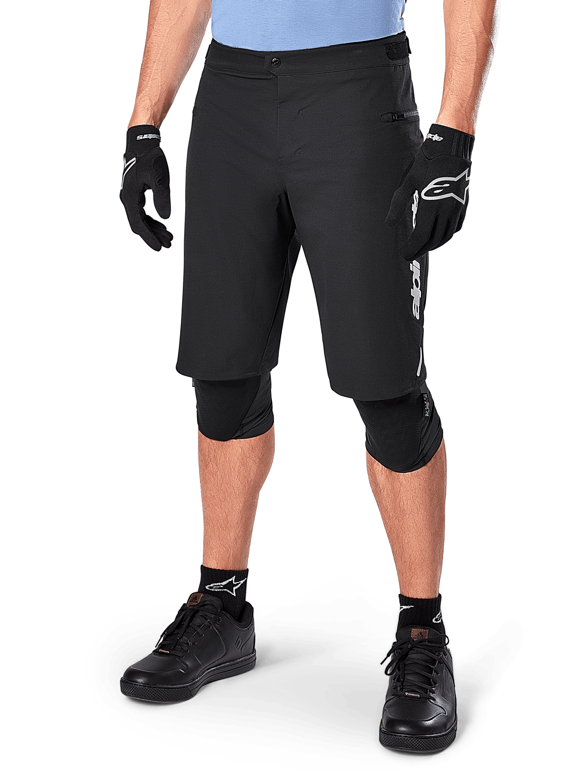 Alpinestars A-Dura Elite Shorts, pantaloncini da MTB neri, indossati con maglia azzurra e protezioni per le ginocchia nere, con chiusura a scatto sicura e tasca con zip, abbinati a scarpe da ciclismo e guanti neri per un completo outfit da fuoristrada.