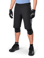 Alpinestars A-Dura Elite Shorts, pantaloncini da MTB neri, indossati con maglia azzurra e protezioni per le ginocchia nere, con chiusura a scatto sicura e tasca con zip, abbinati a scarpe da ciclismo e guanti neri per un completo outfit da fuoristrada.