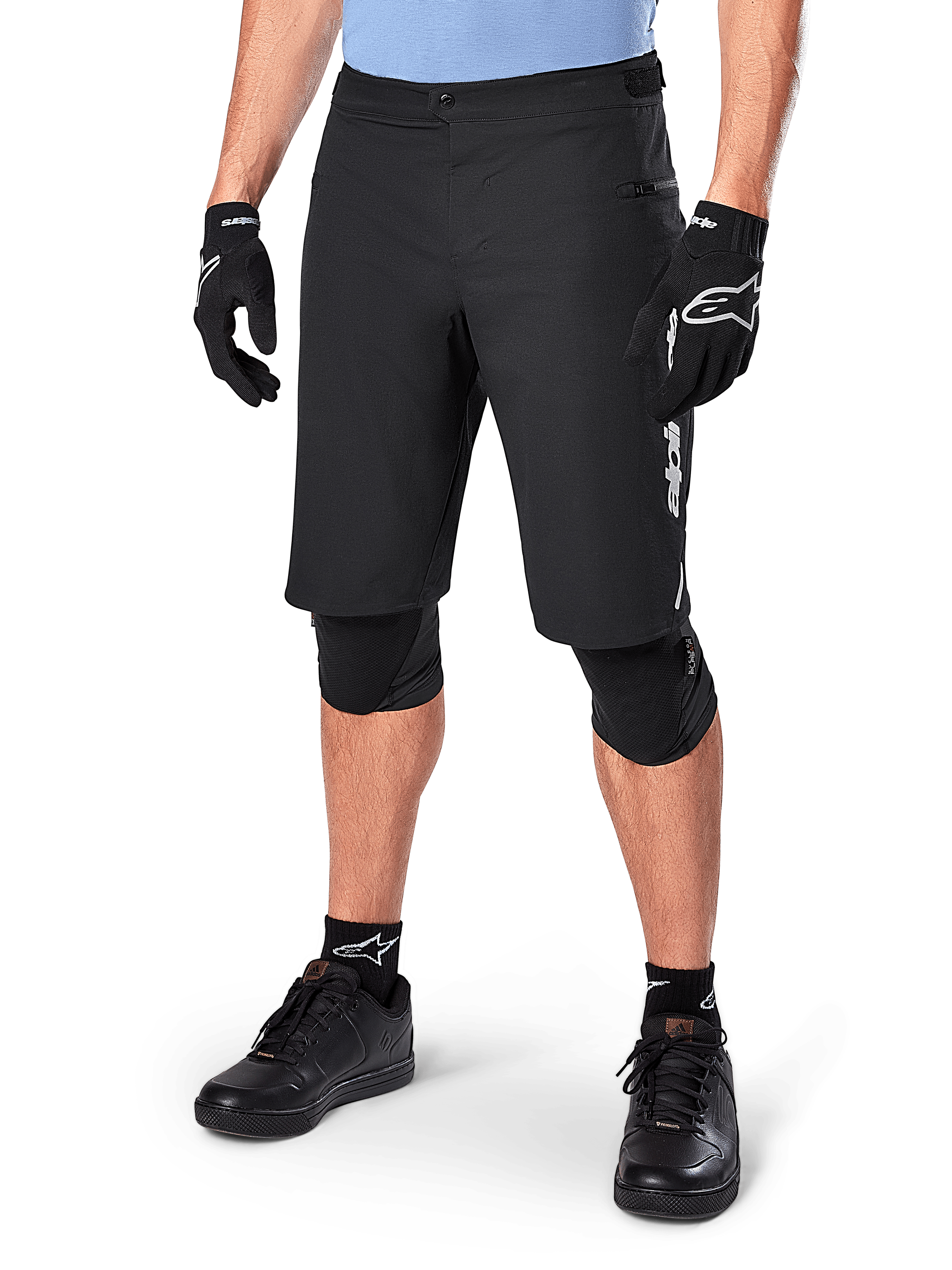 Alpinestars A-Dura Elite Shorts, pantaloncini da MTB neri, indossati con maglia azzurra e protezioni per le ginocchia nere, con chiusura a scatto sicura e tasca con zip, abbinati a scarpe da ciclismo e guanti neri per un completo outfit da fuoristrada.