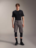 Alpinestars A-Dura Elite Shorts, pantaloncini da mountain bike grigio scuro, indossati con t-shirt nera a girocollo e ginocchiere nere, abbigliamento tecnico da ciclismo lungo fino al ginocchio con chiusura frontale a scatto e resistente tessuto Cordura.