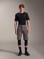 Alpinestars A-Dura Elite Shorts, pantaloncini da mountain bike grigio scuro, indossati con t-shirt nera a girocollo e ginocchiere nere, abbigliamento tecnico da ciclismo lungo fino al ginocchio con chiusura frontale a scatto e resistente tessuto Cordura.