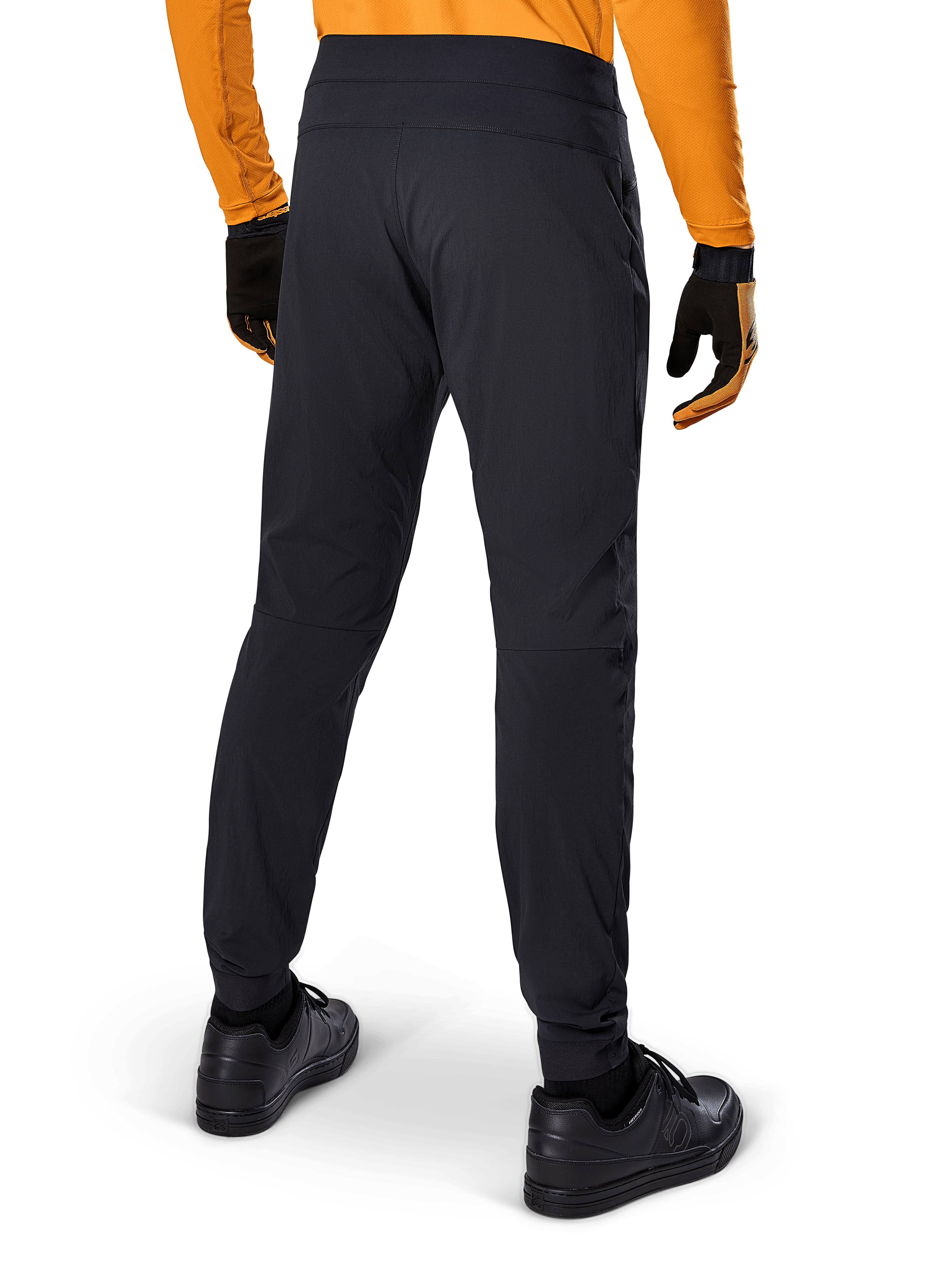 Alpinestars A-Dura Pants, pantaloni MTB neri, vista posteriore, indossati con una maglia a maniche lunghe arancione e guanti neri, con polsini elasticizzati e materiale tessile resistente per la mountain bike.