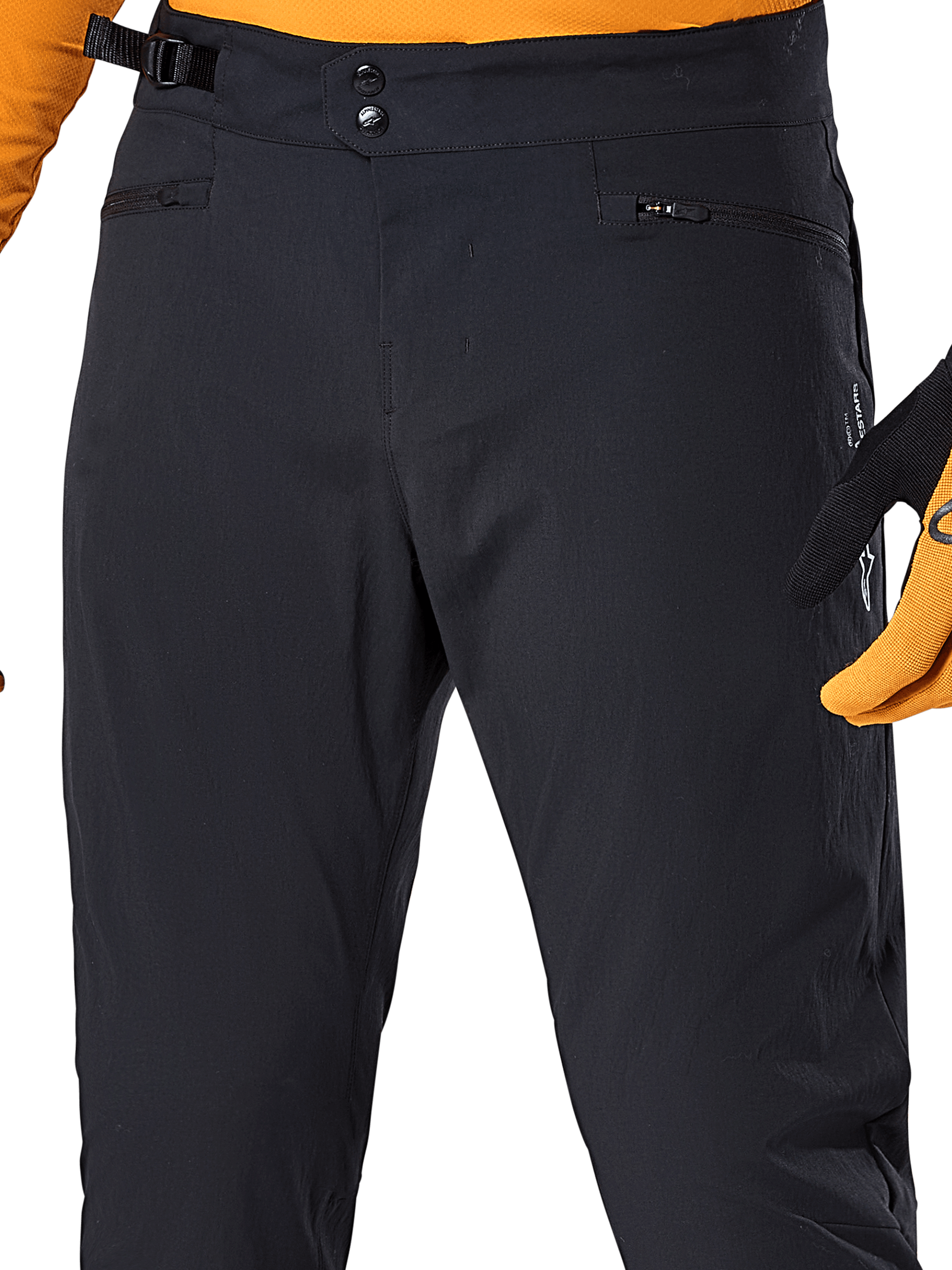 Alpinestars A-Dura Pants, pantaloni da ciclismo MTB neri, vista ravvicinata con doppia chiusura a scatto in vita, regolatore laterale della vita e tasche con cerniera, abbinati a maglia e guanti arancioni