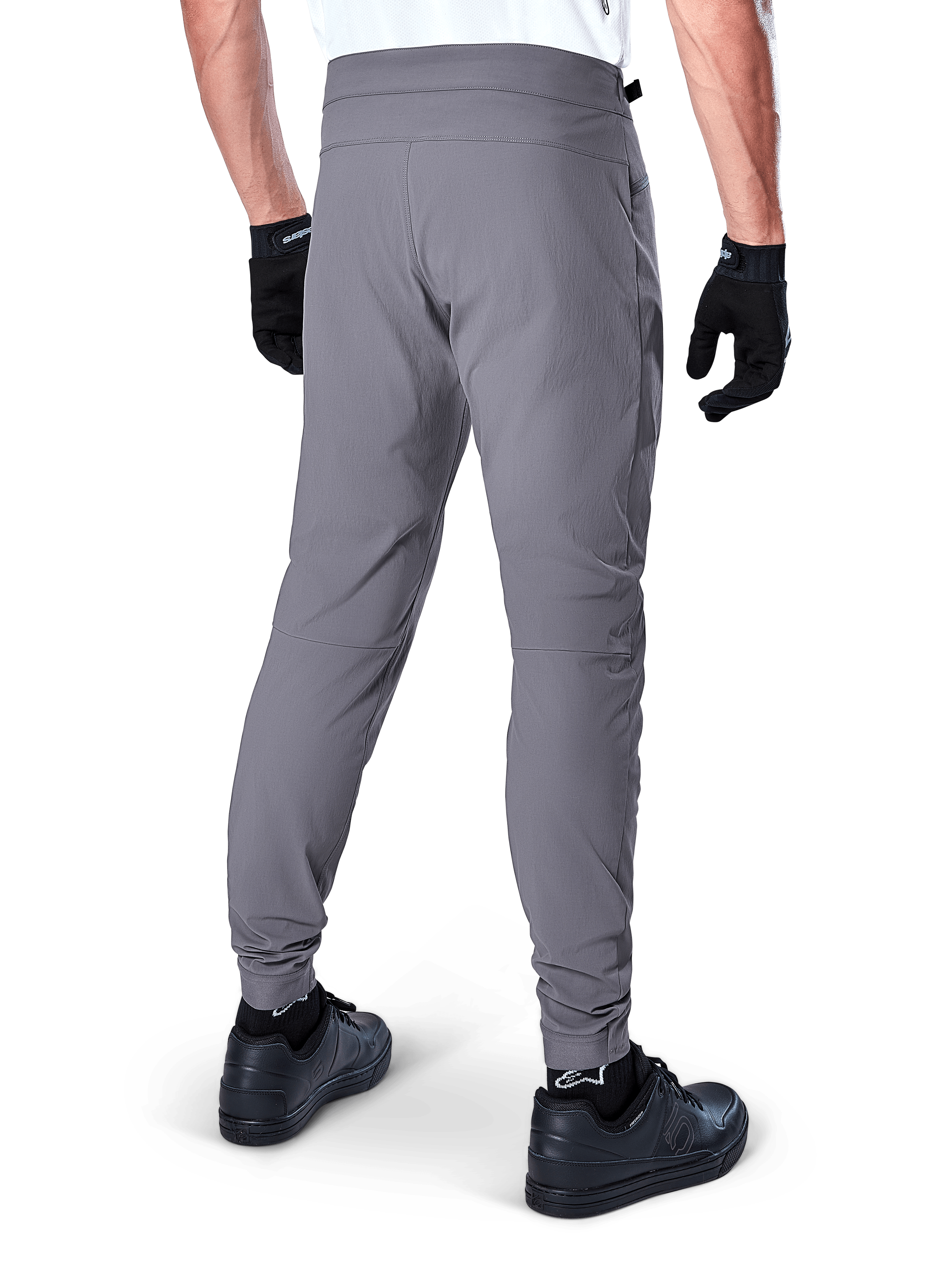 Alpinestars A-Dura Pants, pantaloni da mountain bike, grigio scuro, vista posteriore del modello che indossa l'attrezzatura, con un resistente tessuto elasticizzato in 2 direzioni e polsini elasticizzati, abbinati a guanti e sneaker neri per un look pronto per il ciclismo