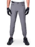 Pantaloni Alpinestars A-Dura, pantaloni da mountain bike grigio scuro, vista frontale indossati con guanti e sneaker neri, con doppia chiusura a scatto in vita, tasche con zip e polsini elasticizzati, abbigliamento da ciclismo resistente per trail riding