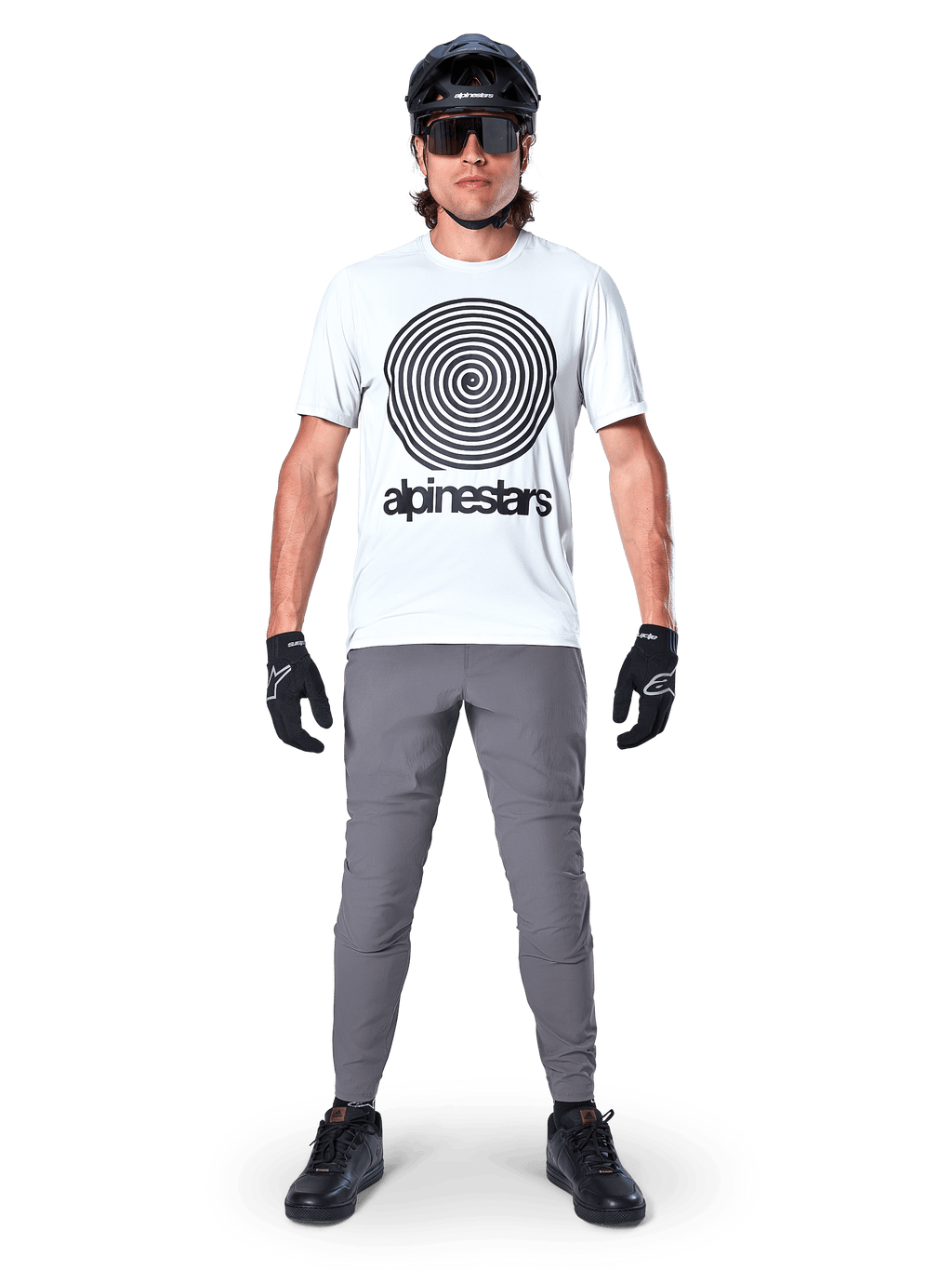 Pantaloni Alpinestars A-Dura, pantaloni da ciclismo MTB, grigio scuro, indossati con una t-shirt grafica bianca, casco nero e guanti, caratterizzati da un design resistente elasticizzato in 2 direzioni e vestibilità regolare per mountain bike