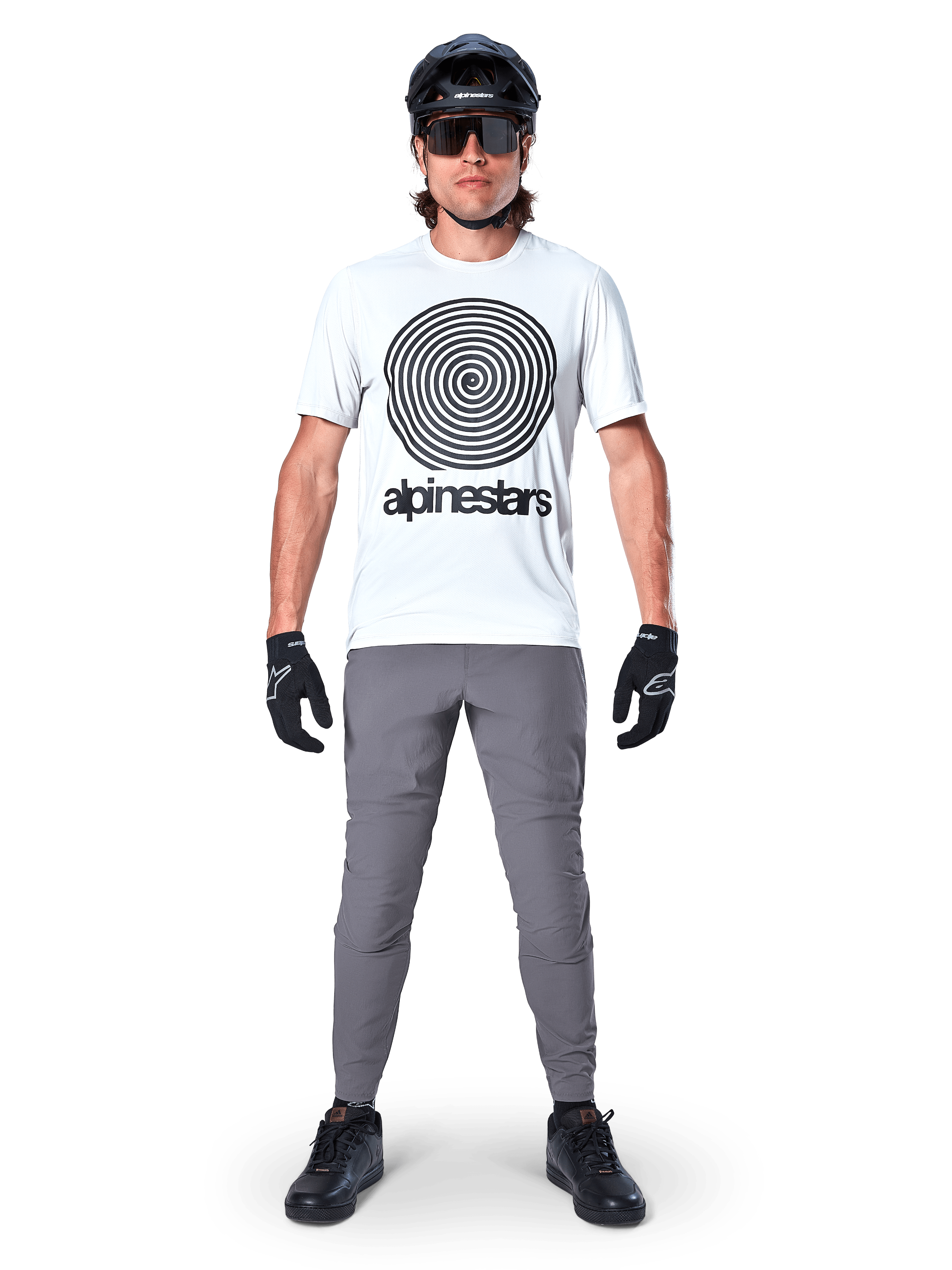 Pantaloni Alpinestars A-Dura, pantaloni da ciclismo MTB, grigio scuro, indossati con una t-shirt grafica bianca, casco nero e guanti, caratterizzati da un design resistente elasticizzato in 2 direzioni e vestibilità regolare per mountain bike