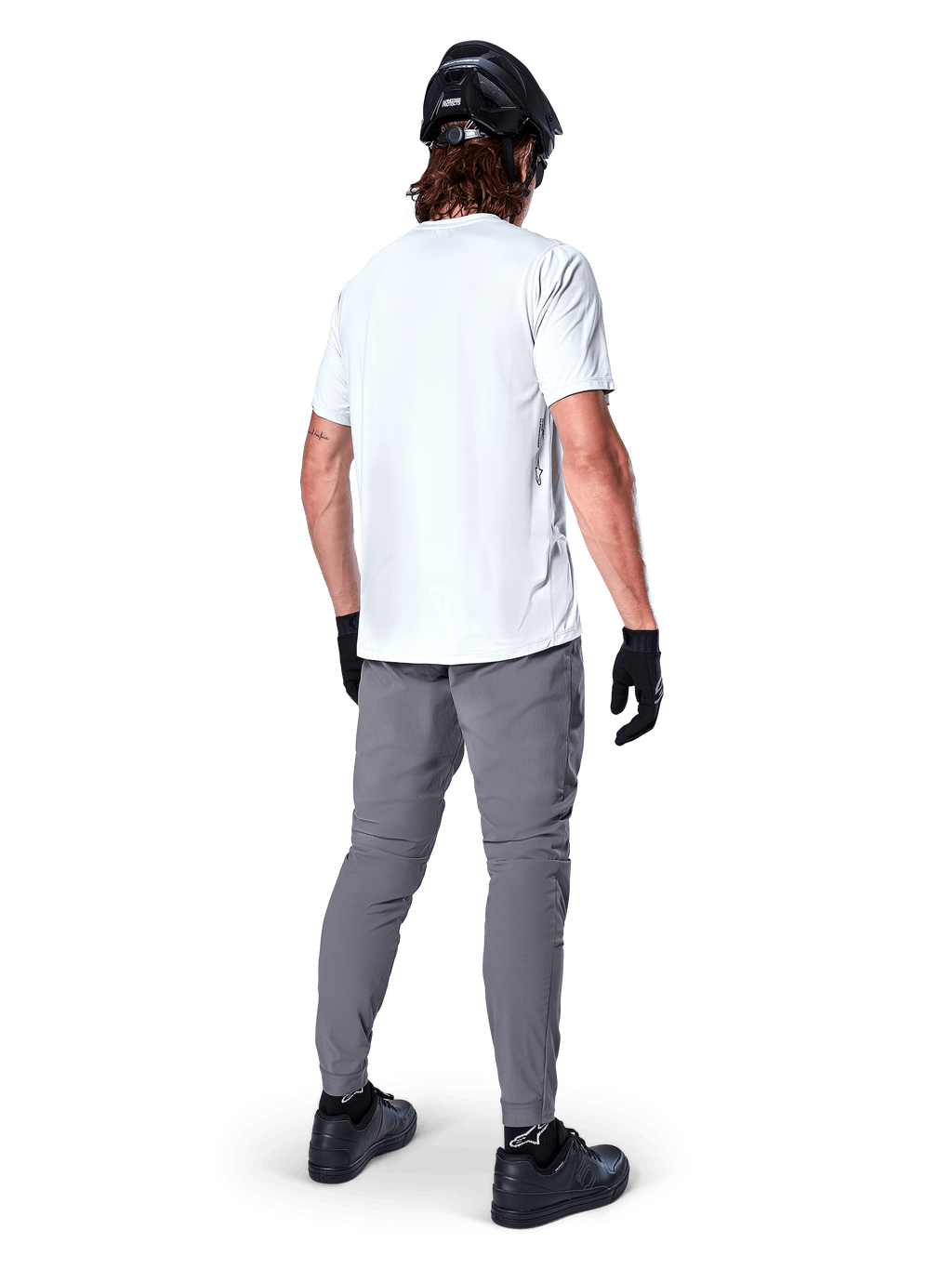 Pantaloni Alpinestars A-Dura, pantaloni da mountain bike grigio scuro visti dal retro, indossati con t-shirt bianca a maniche corte, casco da MTB nero, guanti e scarpe neri, design regular fit con polsini elasticizzati, abbigliamento resistente per ciclismo fuoristrada