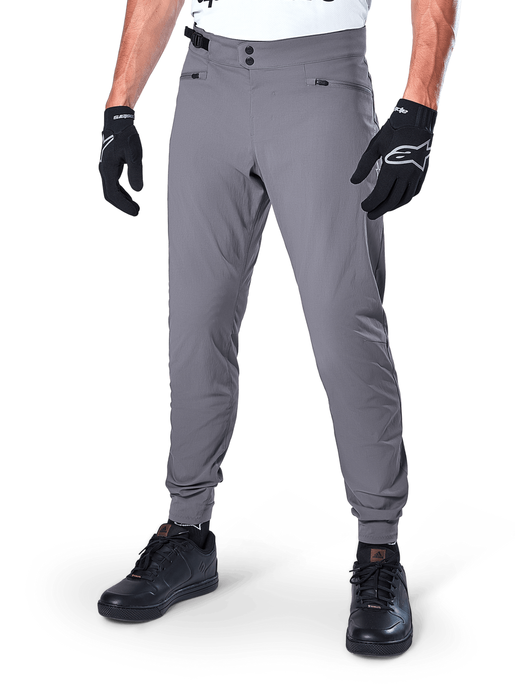 Alpinestars A-Dura Pants, pantaloni MTB grigio scuro, caratterizzati da doppia chiusura a scatto in vita e tasche con cerniera, polsini elasticizzati, indossati con guanti da ciclismo neri e sneakers nere