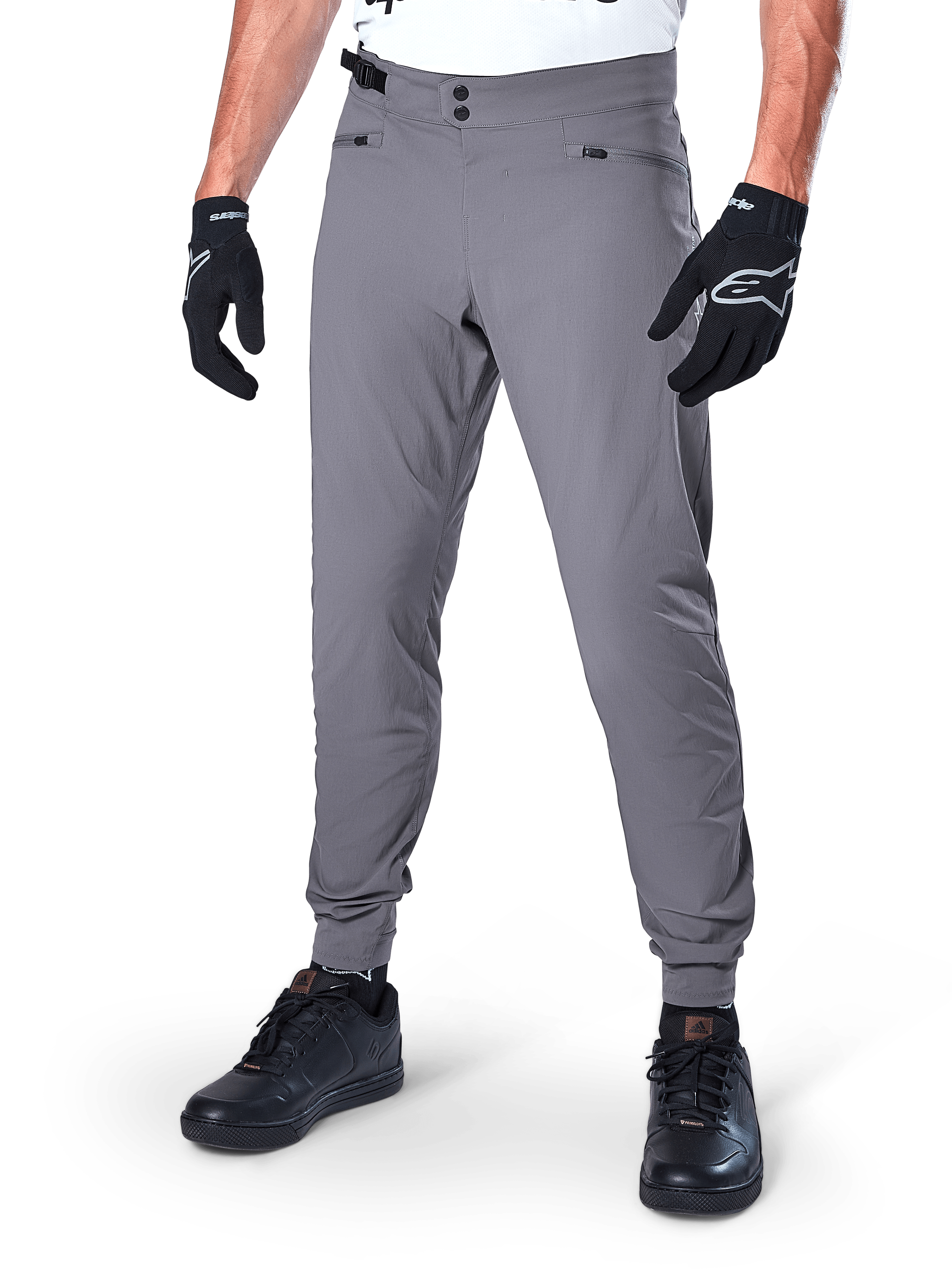 Alpinestars A-Dura Pants, pantaloni MTB grigio scuro, caratterizzati da doppia chiusura a scatto in vita e tasche con cerniera, polsini elasticizzati, indossati con guanti da ciclismo neri e sneakers nere