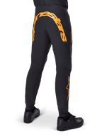 Pantaloni Alpinestars A-Supra Race, pantaloni MTB neri, vista posteriore con grande scritta Alpinestars arancione sul retro, logo arancione sulla parte inferiore della gamba, vestibilità performante con tasca con zip, indossati con scarpe nere