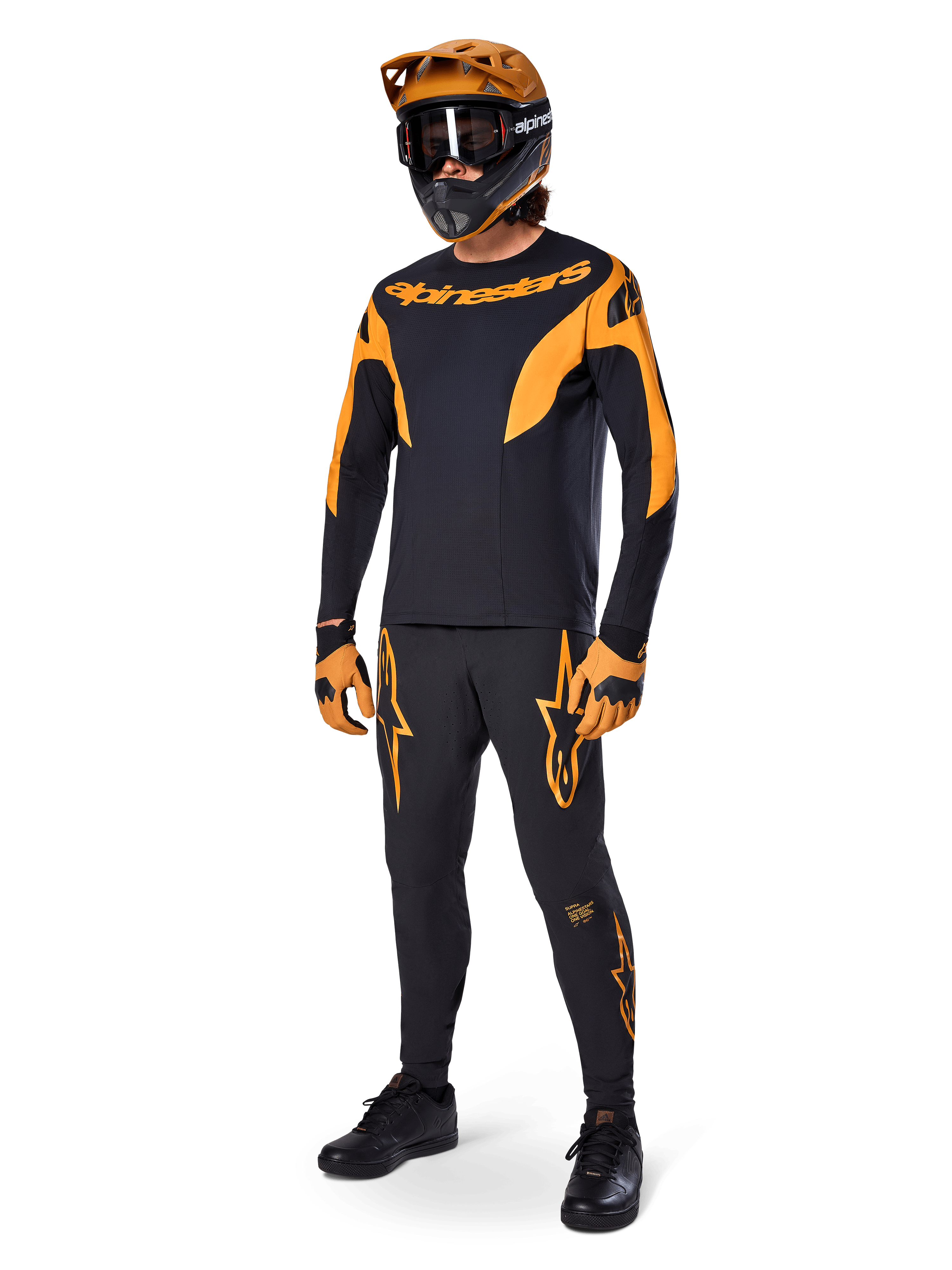 Ciclista di mountain bike con abbigliamento completo da gara, pantaloni Alpinestars A-Supra Race in nero con dettagli arancioni, maglia a maniche lunghe coordinata nera e arancione, casco arancione con maschera nera, guanti arancioni e neri e scarpe nere, design professionale per kit da gara MTB