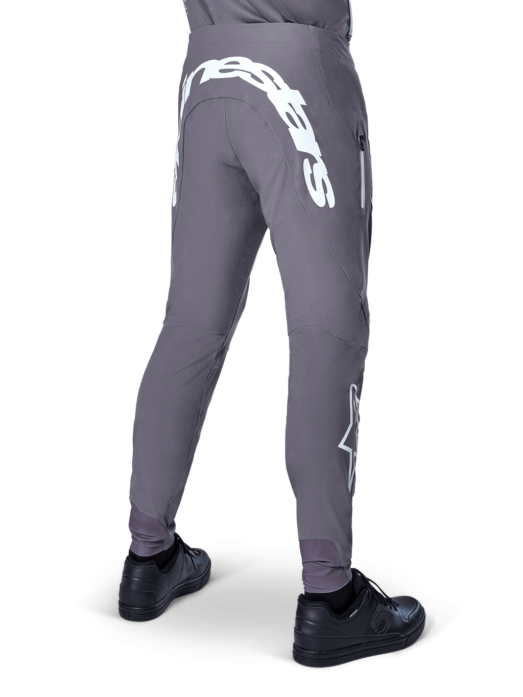 Alpinestars A-Supra Race Pants, pantaloni da mountain bike, grigio scuro, vista posteriore indossati con scarpe nere, caratterizzati da una grande scritta Alpinestars bianca sulla parte posteriore e logo a stella sulla gamba, tasca con zip, tessuto elasticizzato ad alte prestazioni per gare MTB