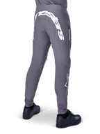 Alpinestars A-Supra Race Pants, pantaloni da mountain bike, grigio scuro, vista posteriore indossati con scarpe nere, caratterizzati da una grande scritta Alpinestars bianca sulla parte posteriore e logo a stella sulla gamba, tasca con zip, tessuto elasticizzato ad alte prestazioni per gare MTB