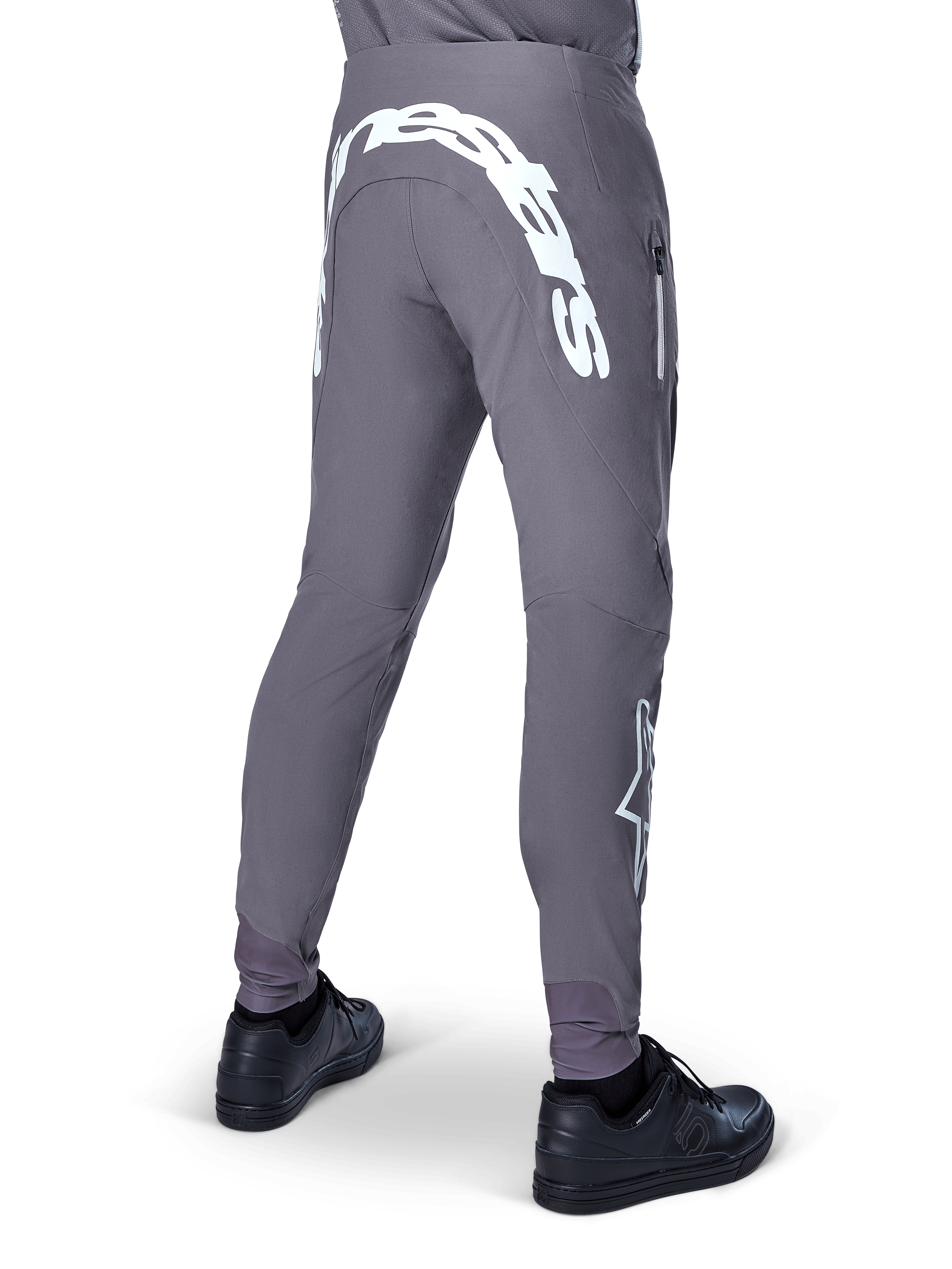 Alpinestars A-Supra Race Pants, pantaloni da mountain bike, grigio scuro, vista posteriore indossati con scarpe nere, caratterizzati da una grande scritta Alpinestars bianca sulla parte posteriore e logo a stella sulla gamba, tasca con zip, tessuto elasticizzato ad alte prestazioni per gare MTB