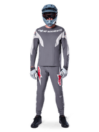 Rider MTB con pantaloni Alpinestars A-Supra Race in grigio scuro, caratterizzati da vivaci loghi rossi sulle cosce, abbinati a maglia grigia coordinata, casco integrale blu e scarpe nere per un kit completo da gara off-road.