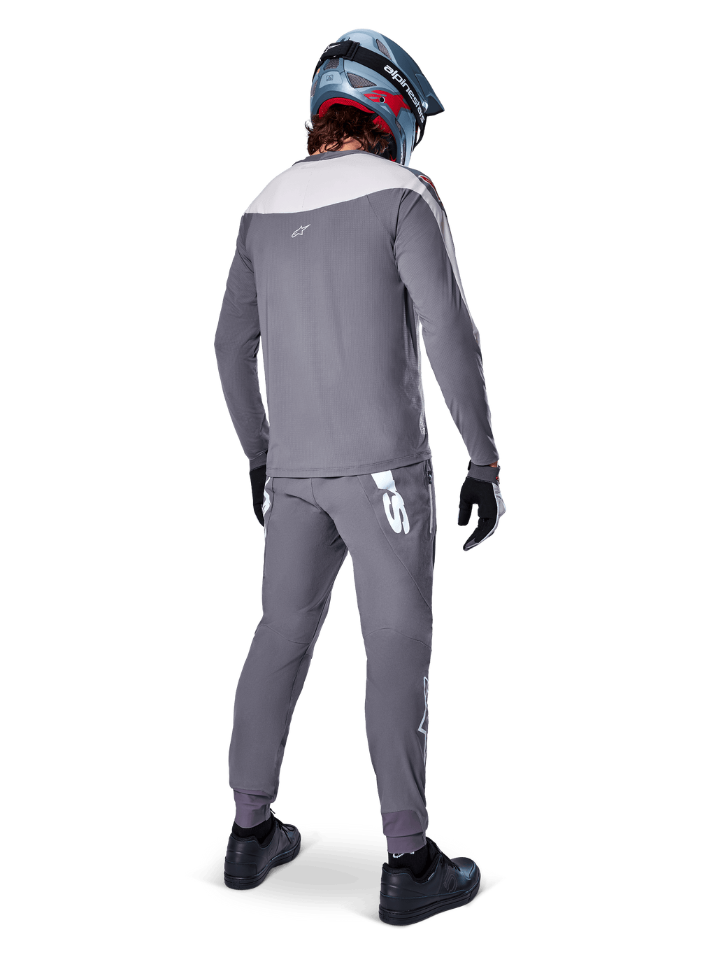 Alpinestars A-Supra Race Pants, grigio scuro, ciclista di mountain bike visto da dietro con kit completo da gara, maglia grigia a maniche lunghe, pantaloni con logo bianco d'ispirazione MX sul carré posteriore, casco grigio e blu, scarpe nere, progettati per prestazioni MTB