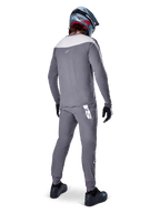 Alpinestars A-Supra Race Pants, grigio scuro, ciclista di mountain bike visto da dietro con kit completo da gara, maglia grigia a maniche lunghe, pantaloni con logo bianco d'ispirazione MX sul carré posteriore, casco grigio e blu, scarpe nere, progettati per prestazioni MTB