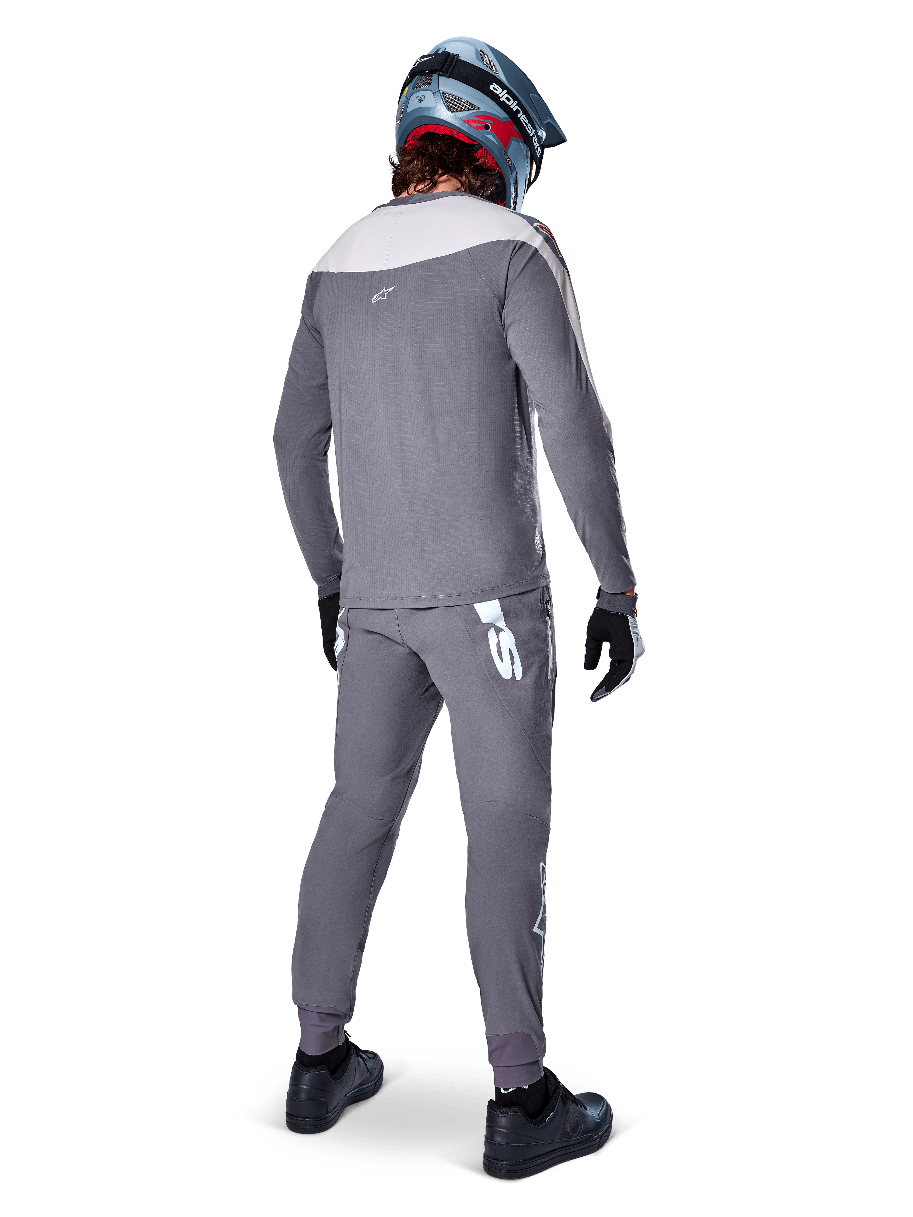 Alpinestars A-Supra Race Pants, grigio scuro, ciclista di mountain bike visto da dietro con kit completo da gara, maglia grigia a maniche lunghe, pantaloni con logo bianco d'ispirazione MX sul carré posteriore, casco grigio e blu, scarpe nere, progettati per prestazioni MTB