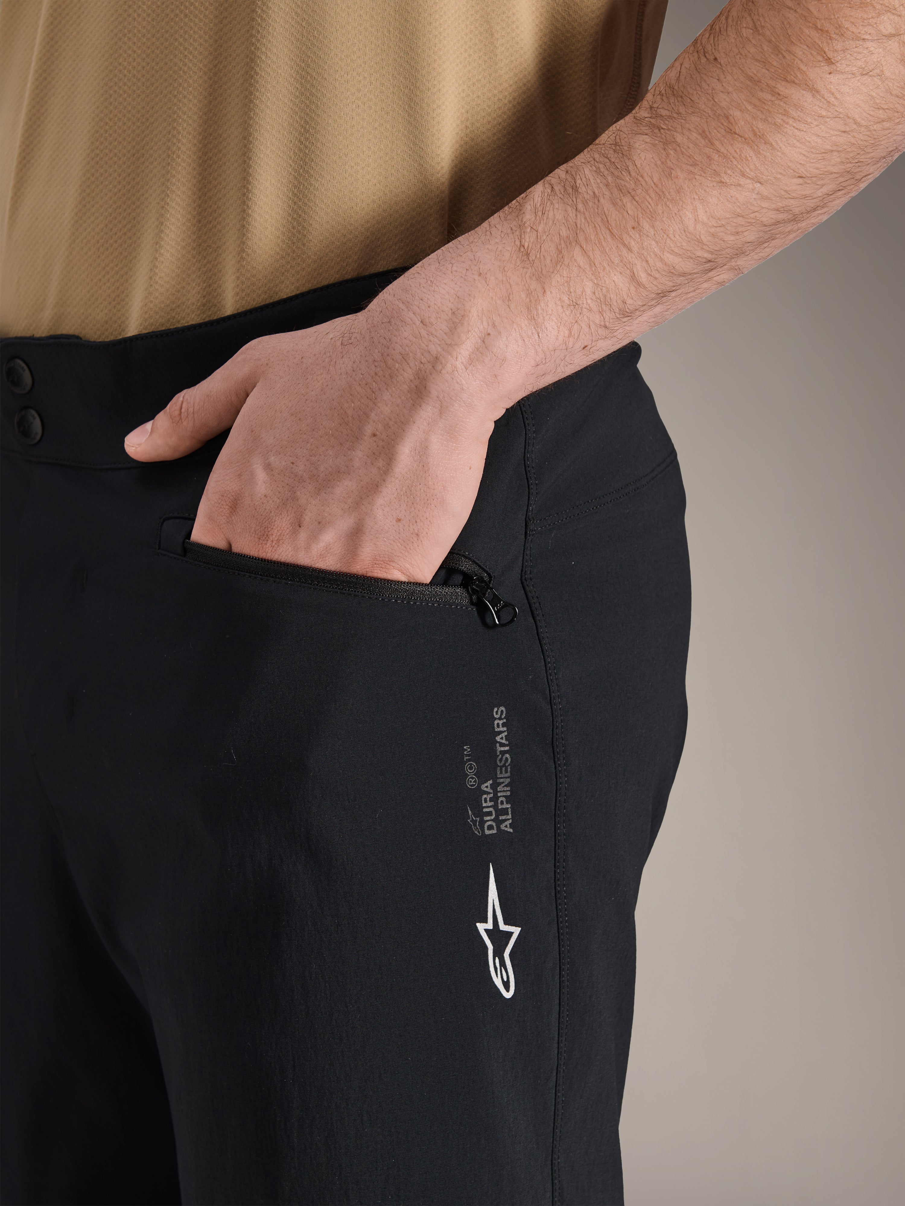 Alpinestars A-Dura Shorts, pantaloncini da mountain bike neri, primo piano della tasca laterale con zip con mano all'interno, logo Alpinestars bianco e marchio A-Dura, tessuto resistente per ciclismo fuoristrada