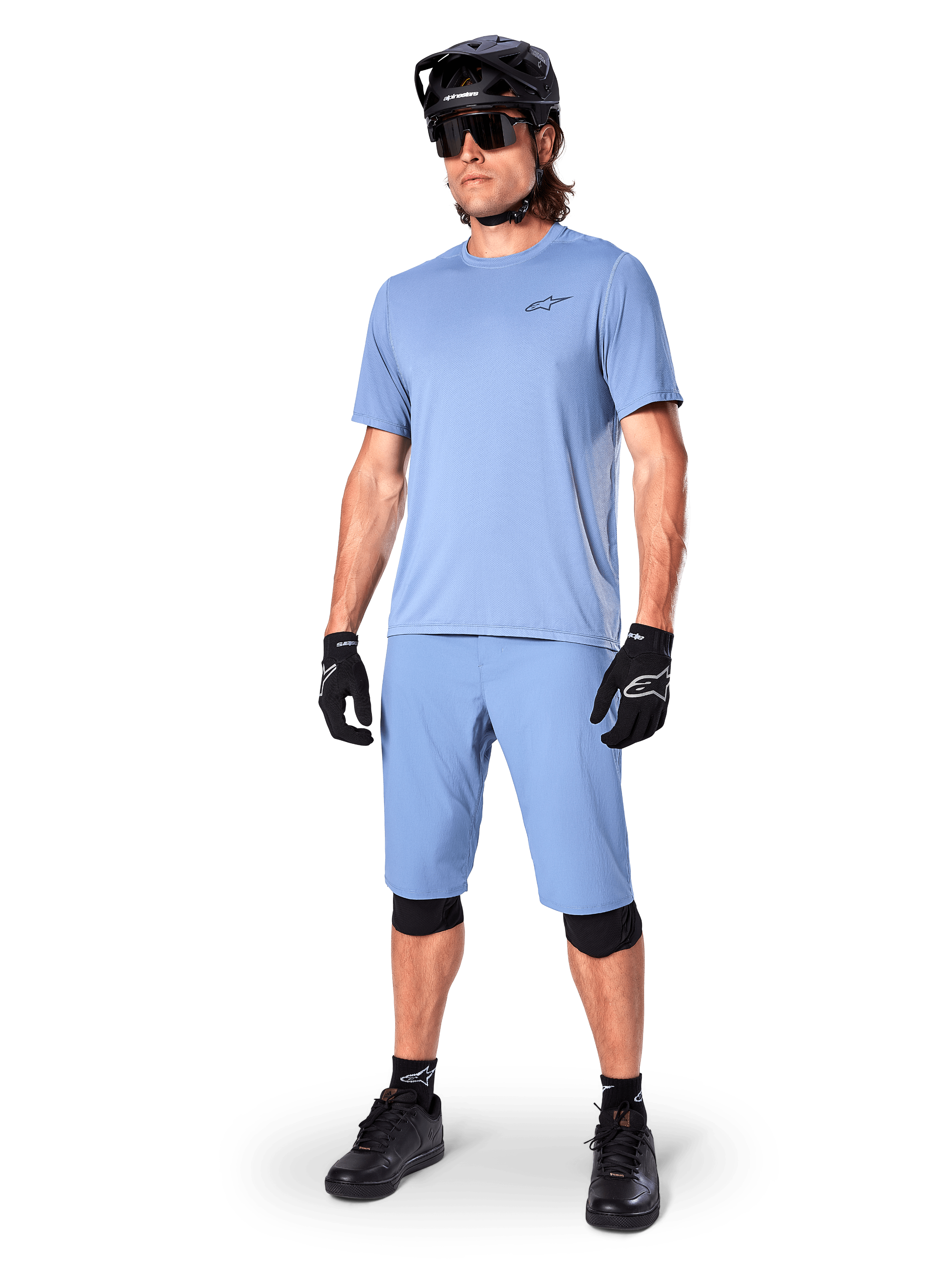 Modello che indossa i pantaloncini Alpinestars A-Dura in Infinity Blue, maglia a maniche corte azzurra coordinata, casco da MTB nero, occhiali da sole e guanti neri, abbigliamento completo da mountain bike per trail riding