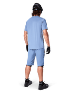 Vista posteriore di un mountain biker con pantaloncini Alpinestars A-Dura in Infinity Blue, maglia a maniche corte coordinata, casco, guanti e scarpe neri, abbigliamento tecnico coordinato per trail riding in MTB