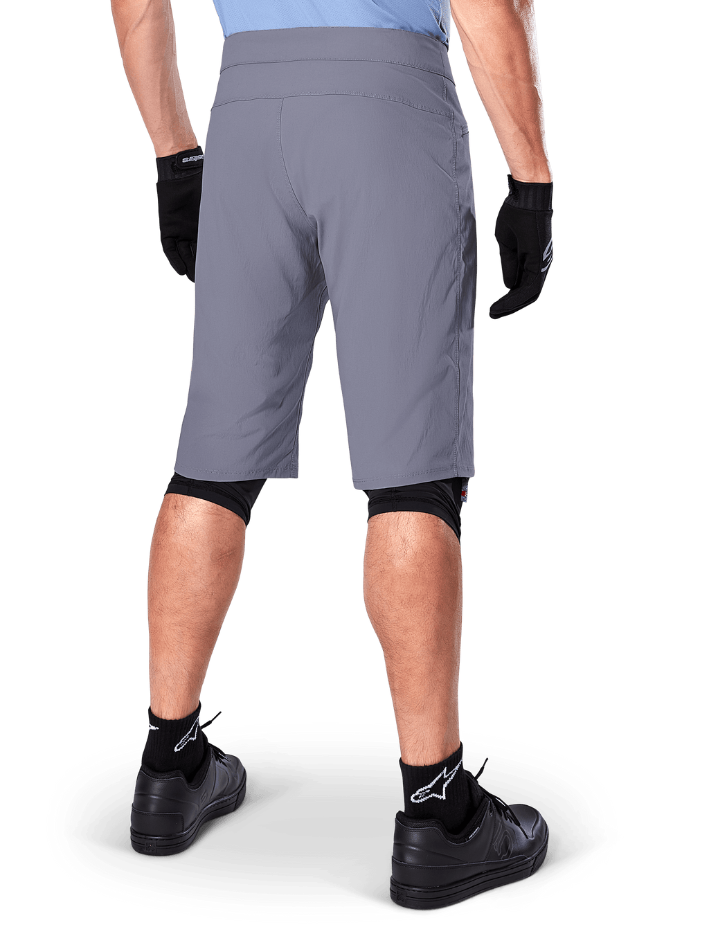 Alpinestars A-Dura Shorts, pantaloncini da mountain bike grigio scuro, vista posteriore su un ciclista, indossati con guanti neri, protezioni ginocchia nere e calze nere con logo Alpinestars, costruzione resistente per il ciclismo fuoristrada