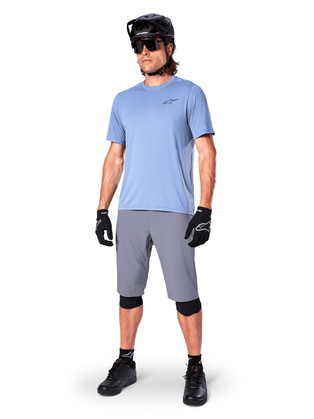 Alpinestars A-Dura Shorts, pantaloncini da MTB, grigio scuro, indossati da un rider con maglia azzurra, casco da MTB nero, guanti neri e ginocchiere, abbigliamento completo da mountain bike per trail e off-road