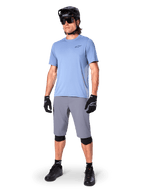 Alpinestars A-Dura Shorts, pantaloncini da MTB, grigio scuro, indossati da un rider con maglia azzurra, casco da MTB nero, guanti neri e ginocchiere, abbigliamento completo da mountain bike per trail e off-road