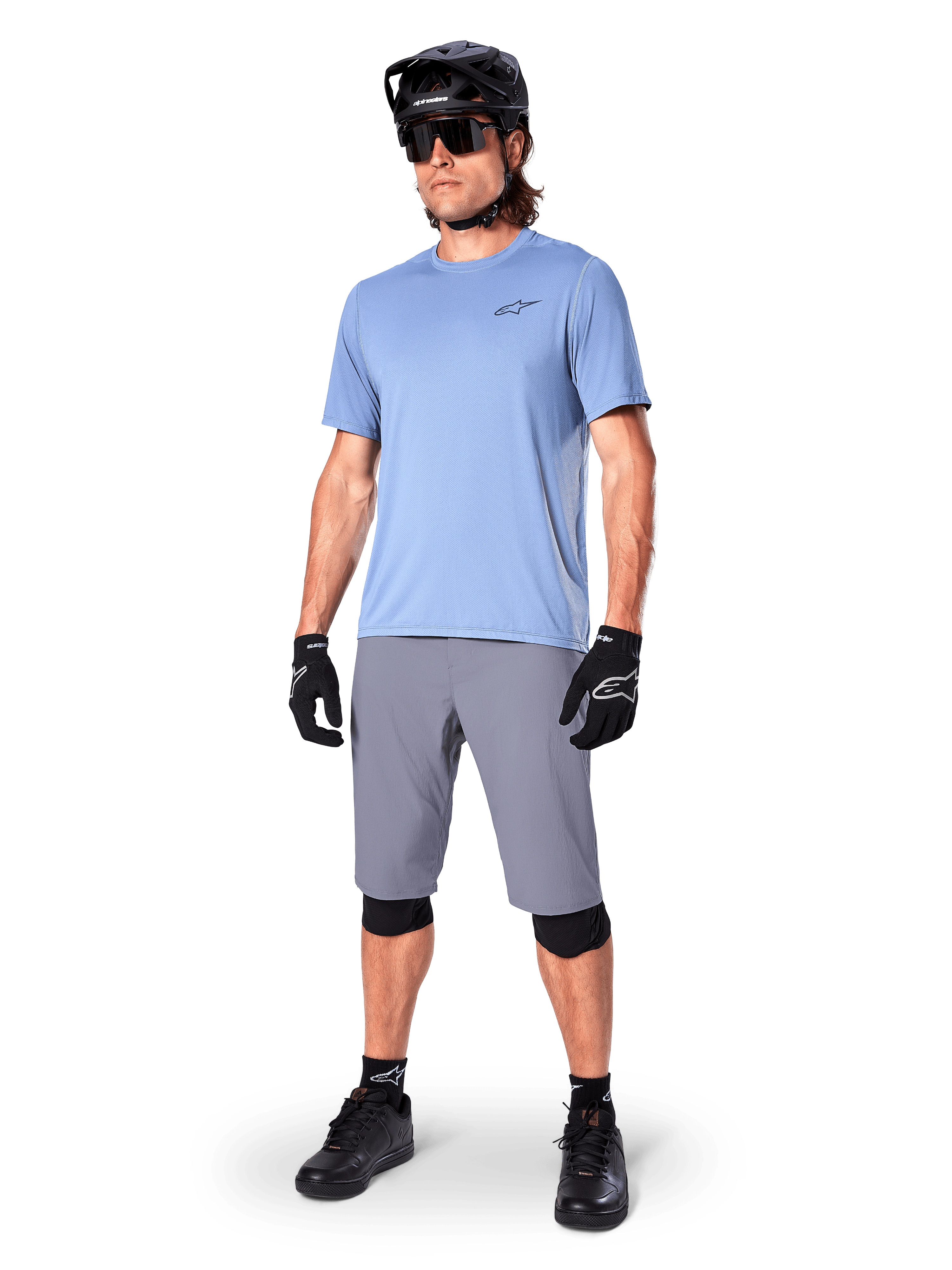 Alpinestars A-Dura Shorts, pantaloncini da MTB, grigio scuro, indossati da un rider con maglia azzurra, casco da MTB nero, guanti neri e ginocchiere, abbigliamento completo da mountain bike per trail e off-road