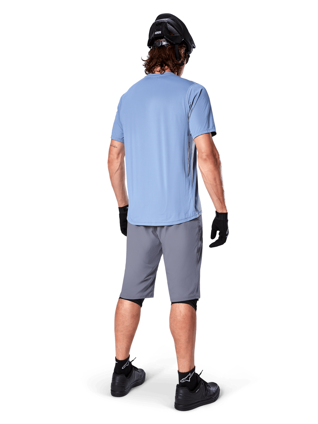 Alpinestars A-Dura Shorts, pantaloncini MTB grigio scuro, vista posteriore, indossati con maglia azzurra a maniche corte e casco da mountain bike nero, guanti e calze neri con scarpe nere, abbigliamento funzionale e resistente per il ciclismo off-road