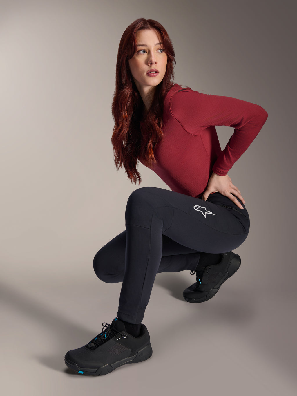 Alpinestars Stella A-Dura Thermal Pants, pantaloni MTB da donna, nero, indossati da una modella in posa accovacciata con maglia bordeaux a maniche lunghe e scarpe da ciclismo nere, logo a stella bianco sulla coscia, struttura calda e resistente per il fuoristrada in climi freddi