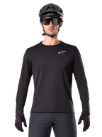 Alpinestars A-Dura Thermal Jersey, maglia da mountain bike a maniche lunghe nera, indossata con casco nero e grandi occhiali da sole, con un piccolo logo Alpinestars bianco sul petto, vestibilità regolare, abbigliamento da ciclismo MTB