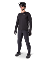 Modello con maglia termica Alpinestars A-Dura, maglia da MTB a maniche lunghe nera, casco da mountain bike nero, occhiali da sole e pantaloni grigio scuro, caratterizzata da un piccolo logo bianco sul petto, struttura in pile isolante per uscite con il freddo