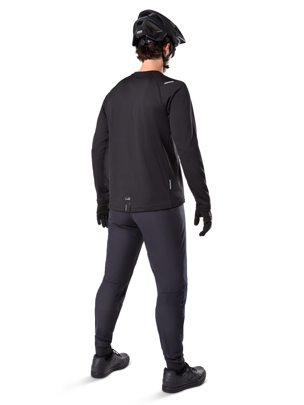 Alpinestars Maglia Termica A-Dura, maglia da ciclismo a maniche lunghe da uomo, nero, vista posteriore su modello con casco MTB nero, pantaloni grigio scuro e guanti neri, abbigliamento professionale da mountain bike per climi freddi