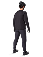 Alpinestars Maglia Termica A-Dura, maglia da ciclismo a maniche lunghe da uomo, nero, vista posteriore su modello con casco MTB nero, pantaloni grigio scuro e guanti neri, abbigliamento professionale da mountain bike per climi freddi