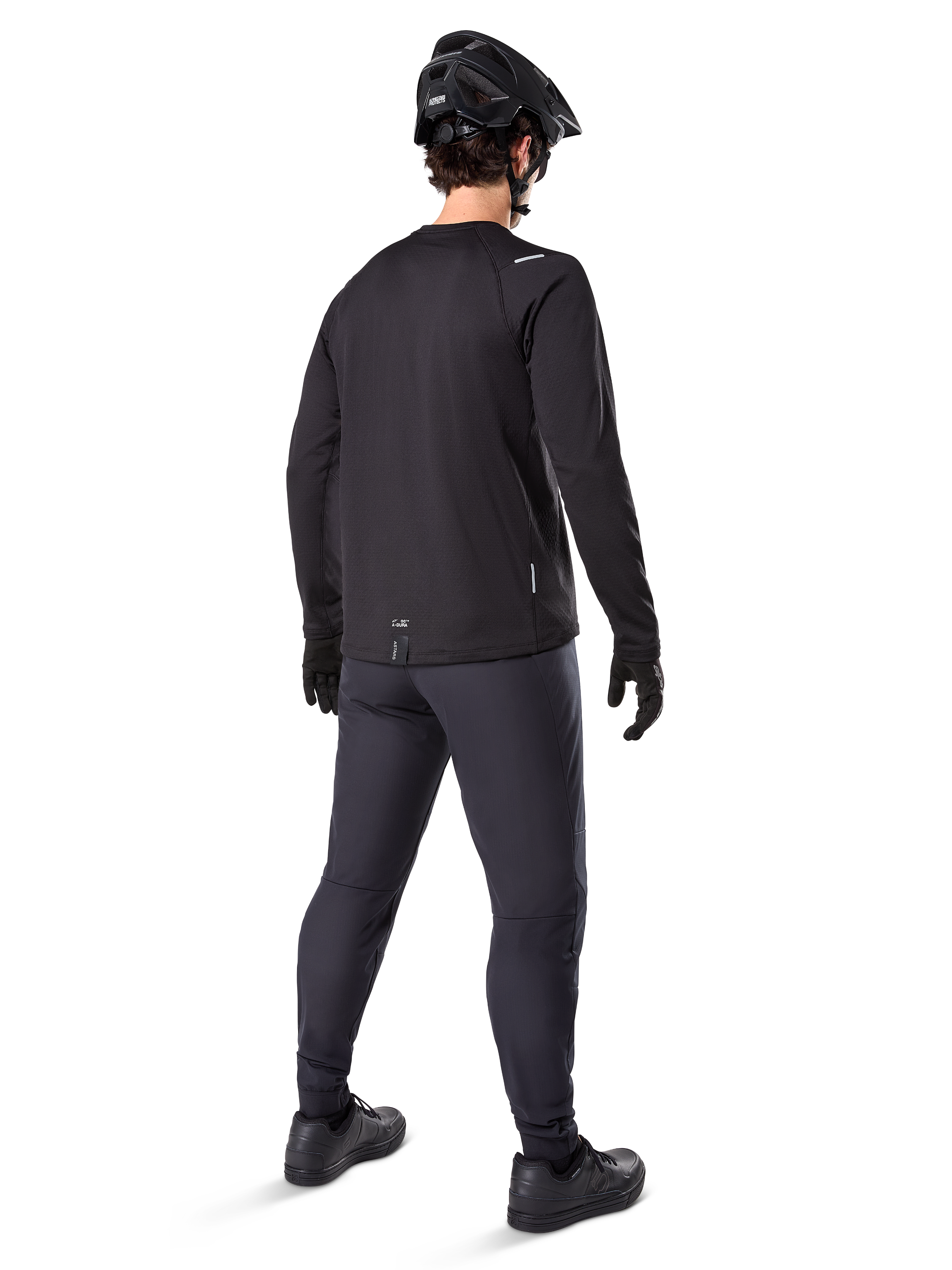 Alpinestars Maglia Termica A-Dura, maglia da ciclismo a maniche lunghe da uomo, nero, vista posteriore su modello con casco MTB nero, pantaloni grigio scuro e guanti neri, abbigliamento professionale da mountain bike per climi freddi