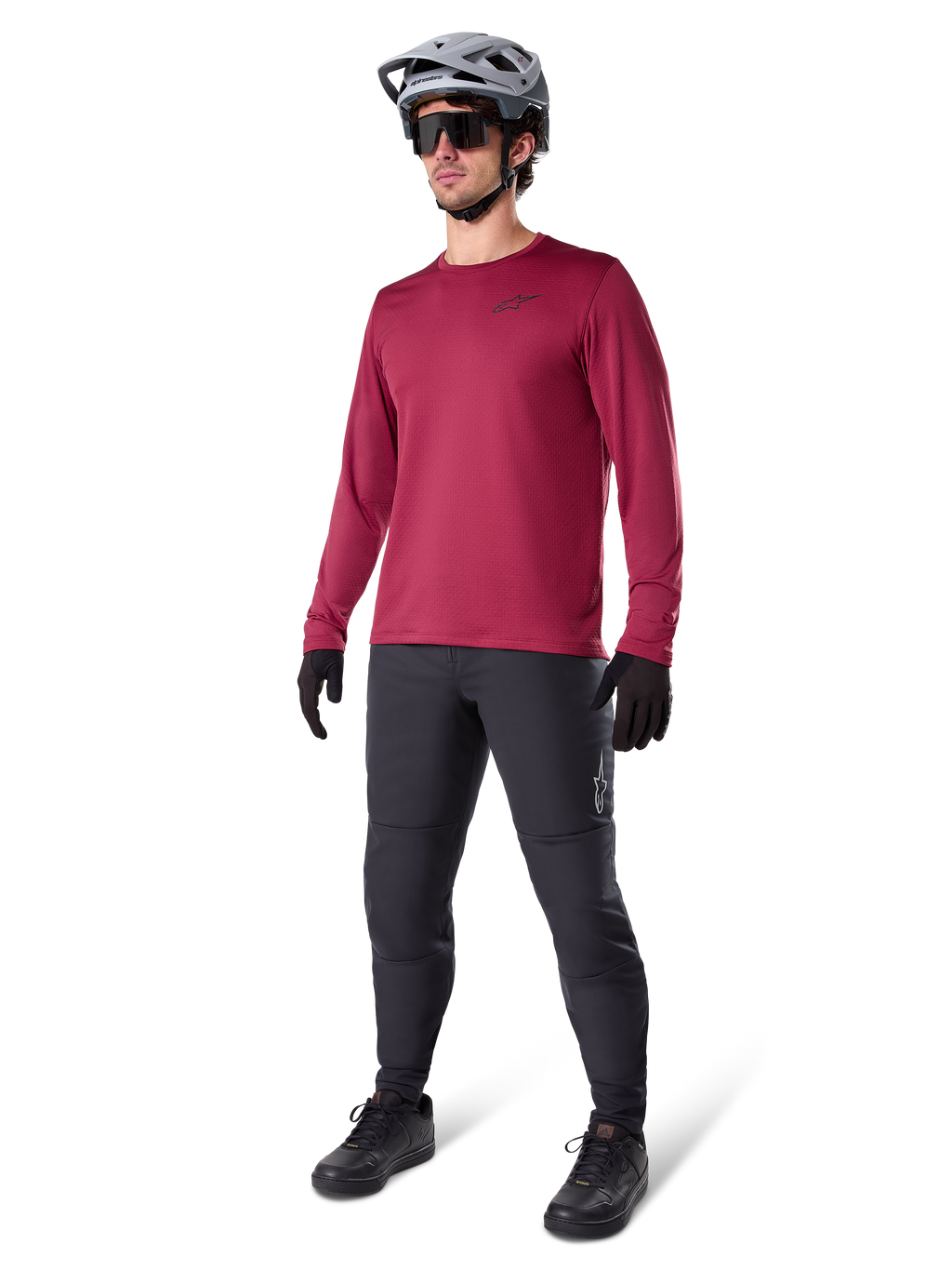 Maglia termica Alpinestars A-Dura in bordeaux, maglia da ciclismo a maniche lunghe isolante, indossata con pantaloni da mountain bike grigio scuro, guanti neri e casco grigio, scatto in studio a figura intera di abbigliamento MTB per il freddo