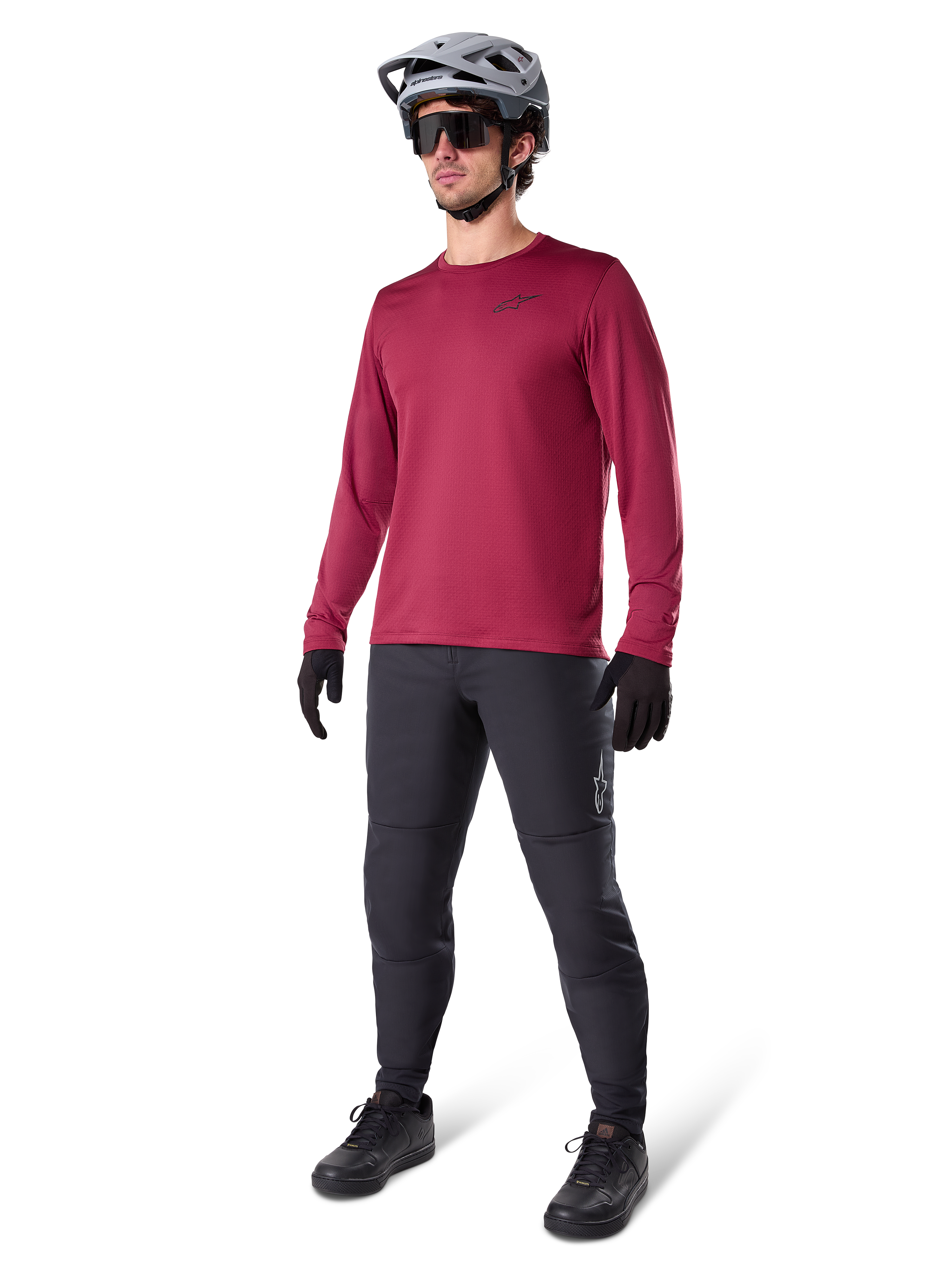 Maglia termica Alpinestars A-Dura in bordeaux, maglia da ciclismo a maniche lunghe isolante, indossata con pantaloni da mountain bike grigio scuro, guanti neri e casco grigio, scatto in studio a figura intera di abbigliamento MTB per il freddo
