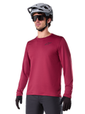 Alpinestars A-Dura Thermal Jersey, maglia da mountain bike a maniche lunghe, rosso burgundy, con fodera in pile isolante e piccolo logo nero sul petto, indossata con casco grigio, occhiali da sole neri e guanti neri, progettata per il ciclismo in climi freddi