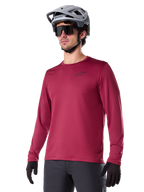 Alpinestars A-Dura Thermal Jersey, maglia da mountain bike a maniche lunghe, rosso burgundy, con fodera in pile isolante e piccolo logo nero sul petto, indossata con casco grigio, occhiali da sole neri e guanti neri, progettata per il ciclismo in climi freddi