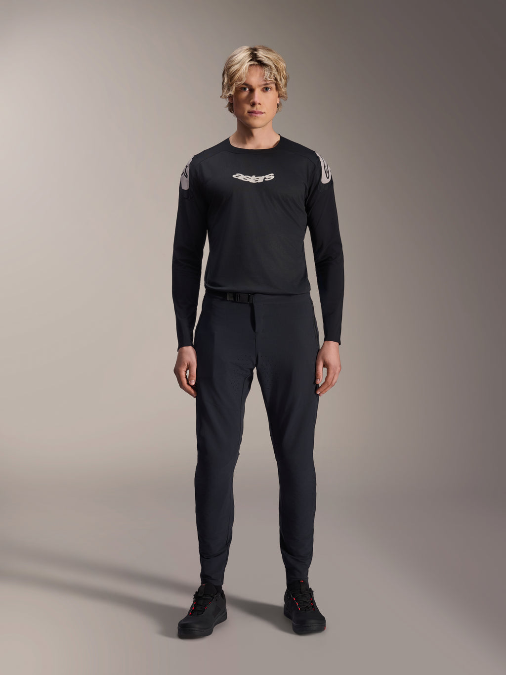 Alpinestars A-Aria Elite Pants, pantaloni da MTB Black Titanium, indossati da un modello con maglia a maniche lunghe coordinata e sneakers, design slim-fit performante con chiusura a fibbia magnetica, abbigliamento tecnico da mountain bike
