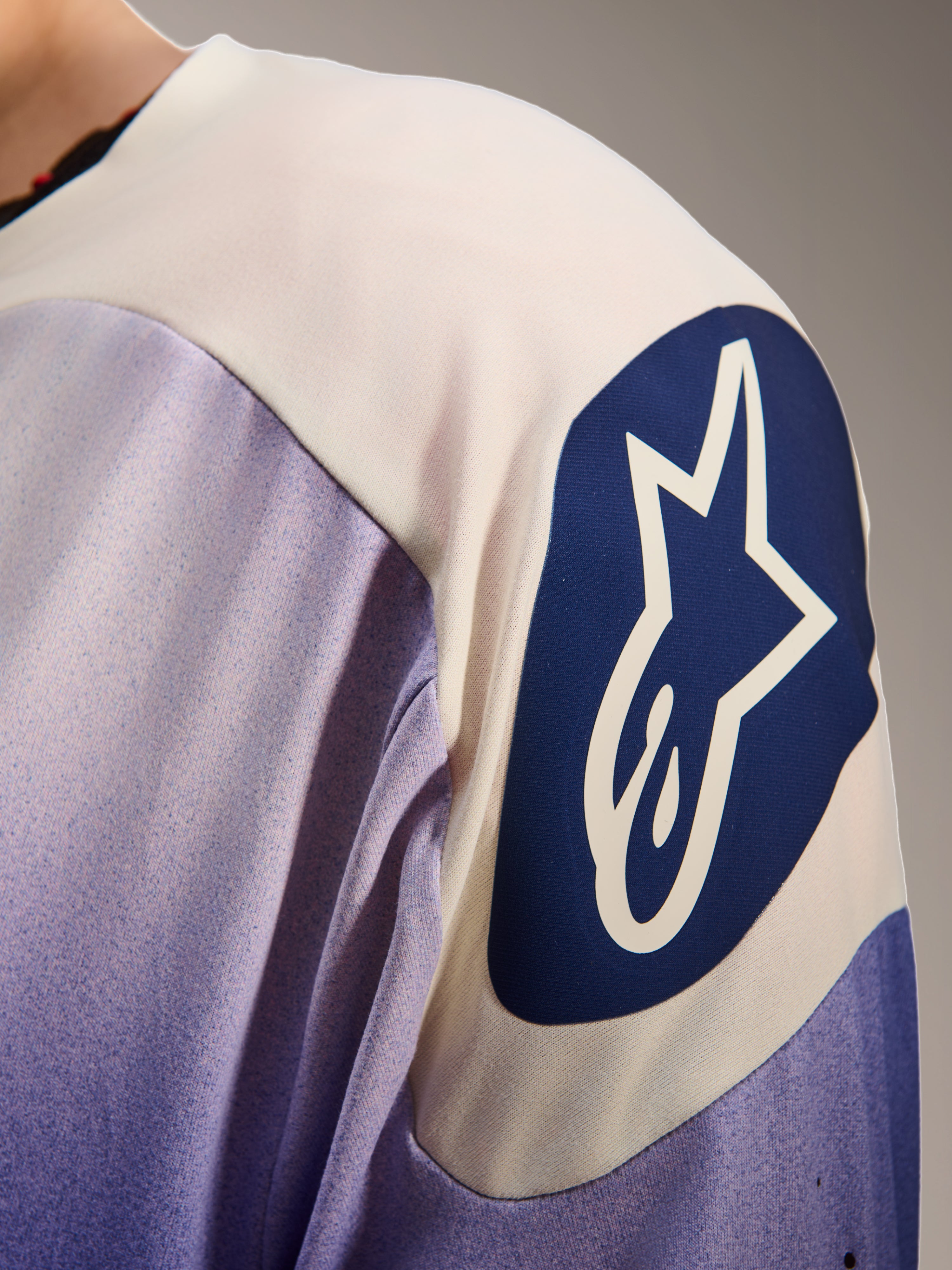 Alpinestars A-Aria Polartec Maker Elite Jersey, maglia da mountain bike a maniche lunghe, Baja Blue e bianco, primo piano della spalla con un grande logo Alpinestars circolare blu con una stella bianca, mostra le perforazioni laser e la trama del tessuto tecnico