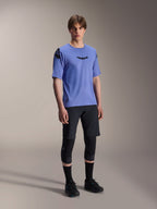 Modello che indossa la maglia a maniche corte Alpinestars A-Aria Polartec Elite in Baja Blue, abbinata a pantaloncini da MTB e ginocchiere neri, con loghi Astars neri sul petto e sulla spalla, abbigliamento tecnico da mountain bike ad alte prestazioni