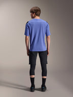 Modello visto da dietro con abbigliamento da mountain bike Alpinestars, maglia a maniche corte A-Aria Polartec Elite azzurra, pantaloncini A-Aria Elite neri, protezioni per le ginocchia nere, calze nere e scarpe nere, completo tecnico coordinato per MTB.